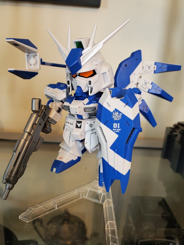 Photo of an SD Hi-Nu Gundam model kit. One of its funnels is in an action pose and the Gundam is holding a gun and a shield.